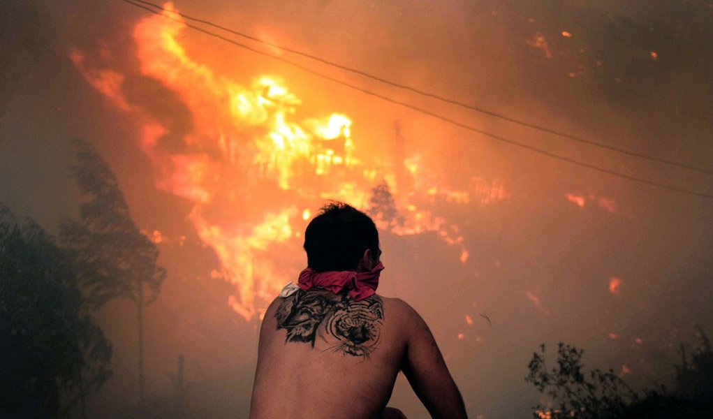 A local stares at houses in flames during a fire in Valparaiso, 110 km west of Santiago, Chile, on April 12, 2014. Authorities decreed a red alert for the area after the fire consumed more than 100 houses. AFP PHOTO / FELIPE GAMBOA (Foto: Roberta Namour) A local stares at houses in flames during a fire in Valparaiso, 110 km west of Santiago, Chile, on April 12, 2014. Authorities decreed a red alert for the area after the fire consumed more than 100 houses. AFP PHOTO / FELIPE GAMBOA