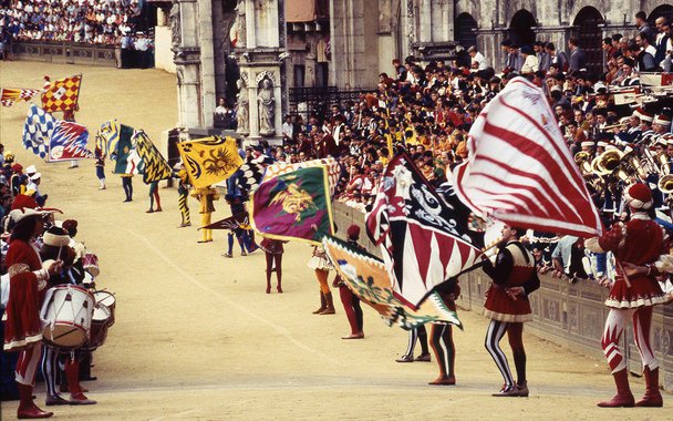 Ritos e festas populares contam a mais colorida, vivaz e brilhante história da cultura e da psicologia dos povos. Isso é particularmente verdadeiro na Itália, cujo acervo de eventos tradicionais do gênero é um dos mais ricos do mundo. Não há dia do ano em que, em algum lugar da Península, a população não saia às ruas para comemorar sagras agrícolas, esportivas, religiosas, culturais. A maior parte dessas celebrações tem origem muito antiga, e muitas remontam inclusive aos tempos pré-cristãos. Na foto de abertura, o Pálio de Siena.
(Foto: Luis Pellegrini)
Ritos e festas populares contam a mais colorida, vivaz e brilhante história da cultura e da psicologia dos povos. Isso é particularmente verdadeiro na Itália, cujo acervo de eventos tradicionais do gênero é um dos mais ricos do mundo. Não há dia do ano em que, em algum lugar da Península, a população não saia às ruas para comemorar sagras agrícolas, esportivas, religiosas, culturais. A maior parte dessas celebrações tem origem muito antiga, e muitas remontam inclusive aos tempos pré-cristãos. Na foto de abertura, o Pálio de Siena.