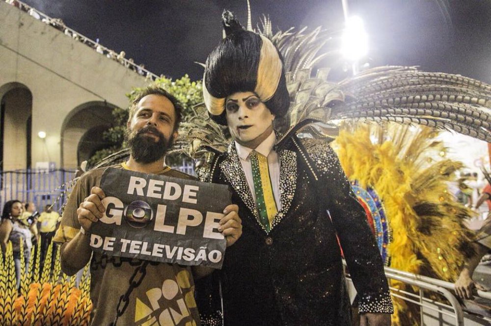 A intervenção militar no Rio de Janeiro já fez sua primeira vítima: a Paraíso do Tuiuti; no desfile das campeãs, o vampirão desfilou sem faixa presidencial; em entrevista à Mídia Ninja, o historiador Léo Morais, que deu vida ao "vampirão", afirmou que seu personagem representa o "sistema" – e não necessariamente Michel Temer, que usurpou a presidência da República por meio de um golpe parlamentar; no desfile, as arquibancadas foram também tomadas por protestos contra a Globo, peça central no golpe de 2016, que pediu a volta das forças armadas no Rio de Janeiro; vídeo (Foto: Leonardo Attuch) A intervenção militar no Rio de Janeiro já fez sua primeira vítima: a Paraíso do Tuiuti; no desfile das campeãs, o vampirão desfilou sem faixa presidencial; em entrevista à Mídia Ninja, o historiador Léo Morais, que deu vida ao "vampirão", afirmou que seu personagem representa o "sistema" – e não necessariamente Michel Temer, que usurpou a presidência da República por meio de um golpe parlamentar; no desfile, as arquibancadas foram também tomadas por protestos contra a Globo, peça central no golpe de 2016, que pediu a volta das forças armadas no Rio de Janeiro; vídeo