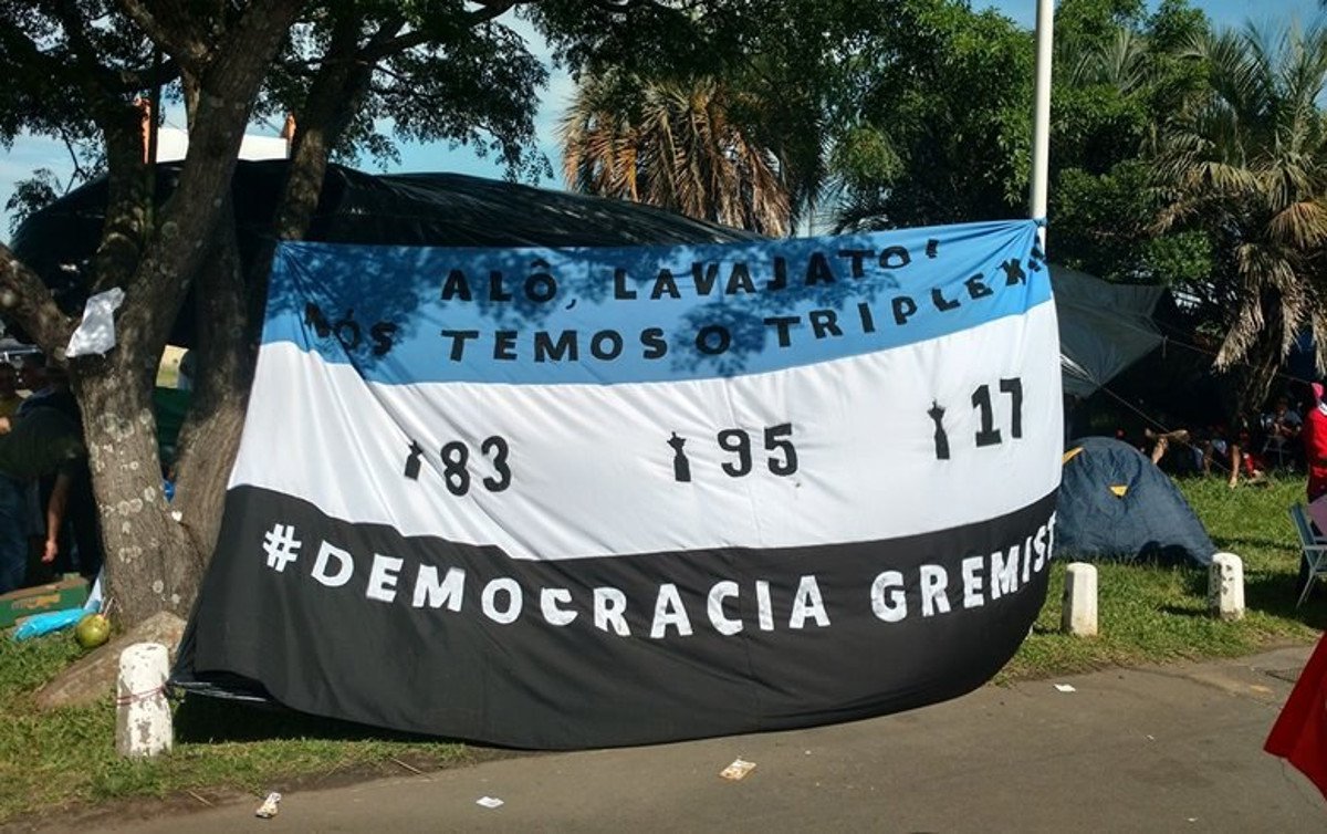 Com bom humor, durante o julgamento dos recursos do ex-presidente Lula, integrantes da Democracia Gremista abriram uma faixa no acampamento montado às margens do rio Guaíba, em Porto Alegre, onde se lê: “Alô Lava Jato, nós temos o tríplex – 83, 95, 2017”, em referência aos três títulos da Libertadores da América conquistados pela equipe gaúcha; “Fizemos essa brincadeira sobre esse momento triste da história política do país, onde querem condenar o Lula sem nenhum tipo de prova. Se não sabem de quem é o tríplex, o tríplex é do Grêmio”, diz Getúlio, um dos fundadores da Democracia Gremista, grupo criado em 2015 para combater a discriminação na torcida gremista (Foto: Charles Nisz) Com bom humor, durante o julgamento dos recursos do ex-presidente Lula, integrantes da Democracia Gremista abriram uma faixa no acampamento montado às margens do rio Guaíba, em Porto Alegre, onde se lê: “Alô Lava Jato, nós temos o tríplex – 83, 95, 2017”, em referência aos três títulos da Libertadores da América conquistados pela equipe gaúcha; “Fizemos essa brincadeira sobre esse momento triste da história política do país, onde querem condenar o Lula sem nenhum tipo de prova. Se não sabem de quem é o tríplex, o tríplex é do Grêmio”, diz Getúlio, um dos fundadores da Democracia Gremista, grupo criado em 2015 para combater a discriminação na torcida gremista