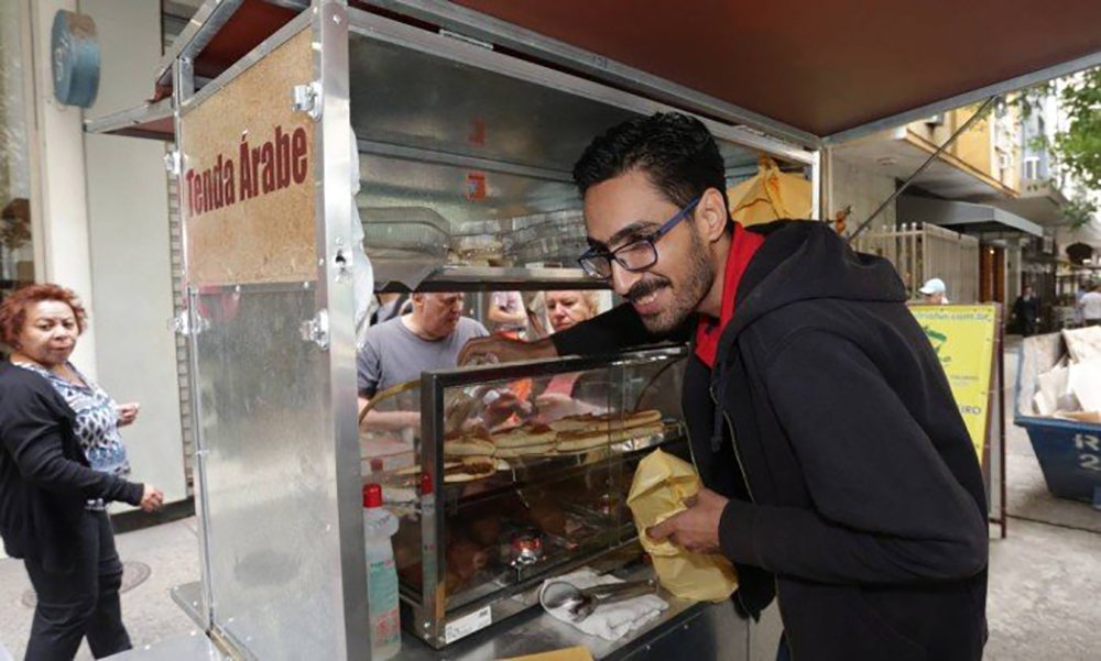 Após o sucesso do 'esfihaço', o refugiado sírio Mohamed Ali Abdelmoatty Ilenavvy, de 33 anos, vítima de xenofobia em Copacabana, pretende comprar um food truck para expandir seu negócio de quitutes além do Rio de Janeiro; convocado nas redes sociais, o ato solidário formou longas filas durante todo o dia de ontem (12) na Rua Santa Clara; "Estou muito feliz. Muito mesmo. Sou a pessoa mais feliz do mundo hoje. E estou muito orgulhoso porque vivo no Brasil, amo todo mundo e fiquei muito surpreso com o movimento. Já perdoei aquele homem (o agressor)", disse Mohamed; ele afirmou que foi o dia mais lucrativo desde que chegou ao Rio, há três anos (Foto: Romulo Faro) Após o sucesso do 'esfihaço', o refugiado sírio Mohamed Ali Abdelmoatty Ilenavvy, de 33 anos, vítima de xenofobia em Copacabana, pretende comprar um food truck para expandir seu negócio de quitutes além do Rio de Janeiro; convocado nas redes sociais, o ato solidário formou longas filas durante todo o dia de ontem (12) na Rua Santa Clara; "Estou muito feliz. Muito mesmo. Sou a pessoa mais feliz do mundo hoje. E estou muito orgulhoso porque vivo no Brasil, amo todo mundo e fiquei muito surpreso com o movimento. Já perdoei aquele homem (o agressor)", disse Mohamed; ele afirmou que foi o dia mais lucrativo desde que chegou ao Rio, há três anos