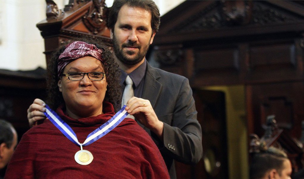 A transexual Gilmara Cunha recebeu, no plenário da Assembleia Legislativa do Rio de Janeiro (Alerj), a Medalha Tiradentes, a maior honraria da Casa; ela é moradora do conjunto de comunidades da Maré, na zona norte do Rio, preside o grupo Conexão G de Cidadania LGBT de Favelas e é integrante do Conselho Nacional de Juventude; "A nossa luta maior é pela sobrevivência dentro dos espaços do território de favelas. Hoje a gente vive uma época de militarização das favelas, então é preciso resistir porque a sobrevivência, a vida em si, desta população precisa ser garantida dentro desse espaço", disse (Foto: Leonardo Lucena) A transexual Gilmara Cunha recebeu, no plenário da Assembleia Legislativa do Rio de Janeiro (Alerj), a Medalha Tiradentes, a maior honraria da Casa; ela é moradora do conjunto de comunidades da Maré, na zona norte do Rio, preside o grupo Conexão G de Cidadania LGBT de Favelas e é integrante do Conselho Nacional de Juventude; "A nossa luta maior é pela sobrevivência dentro dos espaços do território de favelas. Hoje a gente vive uma época de militarização das favelas, então é preciso resistir porque a sobrevivência, a vida em si, desta população precisa ser garantida dentro desse espaço", disse