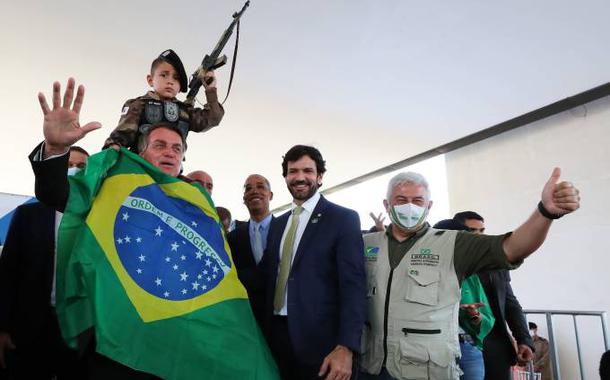 Bolsonaro se enrola na bandeira nacional para foto com criança segurando arma de brinquedo (Foto: Isac Nóbrega/Pr/Divulgação) Bolsonaro se enrola na bandeira nacional para foto com criança segurando arma de brinquedo