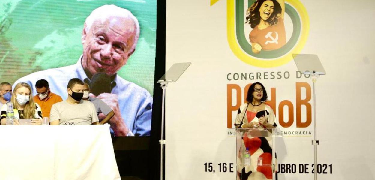 Luciana Santos, presidente do PCdoB. No painel ao fundo, imagem de Haroldo Lima, dirigente do partido falecido em março último, homenageado no congresso