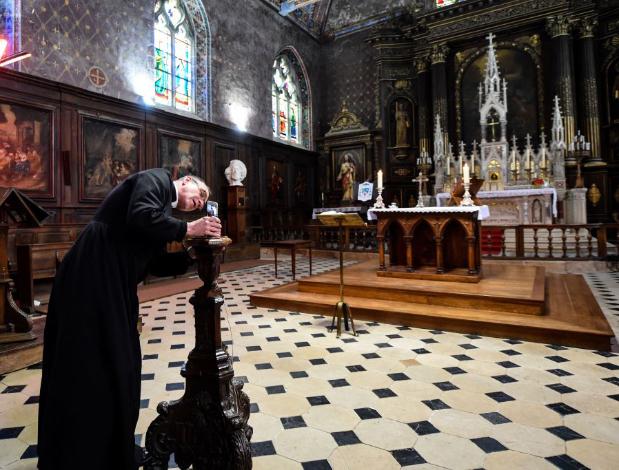Father Olivier Monnier installs his mobile phone on a wooden candlestick as he prepares to broadcast the 11 o'clock Mass with a video chat smart phone application on April 3, 2020, at Saint-Jacques church in Illiers-Combray, France. Father Olivier Monnier installs his mobile phone on a wooden candlestick as he prepares to broadcast the 11 o'clock Mass with a video chat smart phone application on April 3, 2020, at Saint-Jacques church in Illiers-Combray, France.