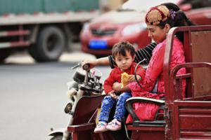 A Uyghur mother and child ride through a busy street in Xinjiang. A Uyghur mother and child ride through a busy street in Xinjiang.