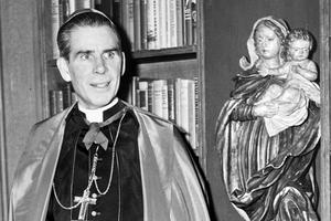Bishop Fulton Sheen stands before a bookcase on the set of his Dumont television program. Bishop Fulton Sheen stands before a bookcase on the set of his Dumont television program.