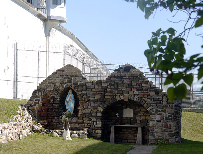 ABOVE: The Lourdes Grotto outside the Church of St. Dismas. BELOW: (1) Ogdensburg Bishop Terry LaValley baptizes an inmate at the Church of St. Dismas. (2) Bishop LaValley and Deacon Frank Bushey with inmates at the Church of St. Dismas in January 2019. ABOVE: The Lourdes Grotto outside the Church of St. Dismas. BELOW: (1) Ogdensburg Bishop Terry LaValley baptizes an inmate at the Church of St. Dismas. (2) Bishop LaValley and Deacon Frank Bushey with inmates at the Church of St. Dismas in January 2019.