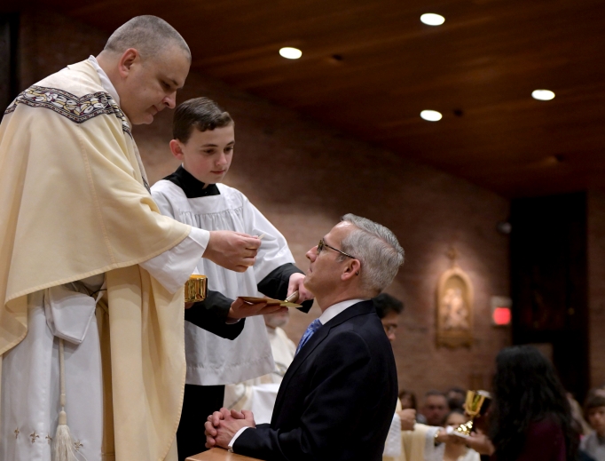 Above, Father John Mosimann, pastor of St. Mary of the Immaculate Conception parish in Fredericksburg, Virginia, gives David Bereit Communion during the Easter vigil Mass. Below, the Bereit family celebrates the new Catholic with Father Mosimann. Above, Father John Mosimann, pastor of St. Mary of the Immaculate Conception parish in Fredericksburg, Virginia, gives David Bereit Communion during the Easter vigil Mass. Below, the Bereit family celebrates the new Catholic with Father Mosimann.