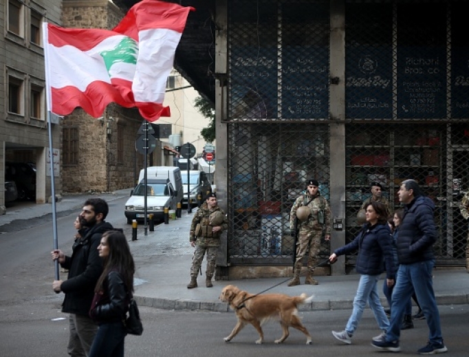 Army soldiers look on as Lebanese anti-government protesters march toward the capital in Beirut's downtown district Jan. 25. The political impasse is worsening an already-dire economic crisis in Lebanon that the World Bank says may see the number of people living in poverty climb from a third to half the population. Army soldiers look on as Lebanese anti-government protesters march toward the capital in Beirut's downtown district Jan. 25. The political impasse is worsening an already-dire economic crisis in Lebanon that the World Bank says may see the number of people living in poverty climb from a third to half the population.