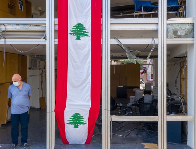 A man stands in the window of a damaged high-rise building, draped with banner in the style of the Lebanese flag, on August 12, 2020 in Beirut, Lebanon. The explosion at Beirut's port last week killed over 200 people, injured thousands, and upended countless lives. There has been little visible support from government agencies to help residents clear debris and help the displaced, although scores of volunteers from around Lebanon have descended on the city to help clean. A man stands in the window of a damaged high-rise building, draped with banner in the style of the Lebanese flag, on August 12, 2020 in Beirut, Lebanon. The explosion at Beirut's port last week killed over 200 people, injured thousands, and upended countless lives. There has been little visible support from government agencies to help residents clear debris and help the displaced, although scores of volunteers from around Lebanon have descended on the city to help clean.