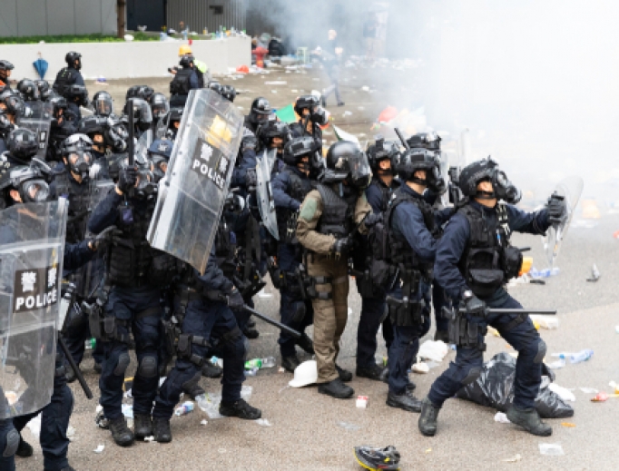 Riot police bunch up next to a cloud of tear gas during clashes with protesters outside the Central Government Office in Hong Kong, June 12, 2019. Riot police bunch up next to a cloud of tear gas during clashes with protesters outside the Central Government Office in Hong Kong, June 12, 2019.