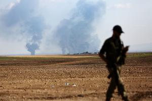 A Turkey-backed Syrian fighter walks as smoke billows in the distance during clashes between Syrian regime forces and Turkish forces near the northeastern town of Ras al-Ein on Oct. 30. A Turkey-backed Syrian fighter walks as smoke billows in the distance during clashes between Syrian regime forces and Turkish forces near the northeastern town of Ras al-Ein on Oct. 30.