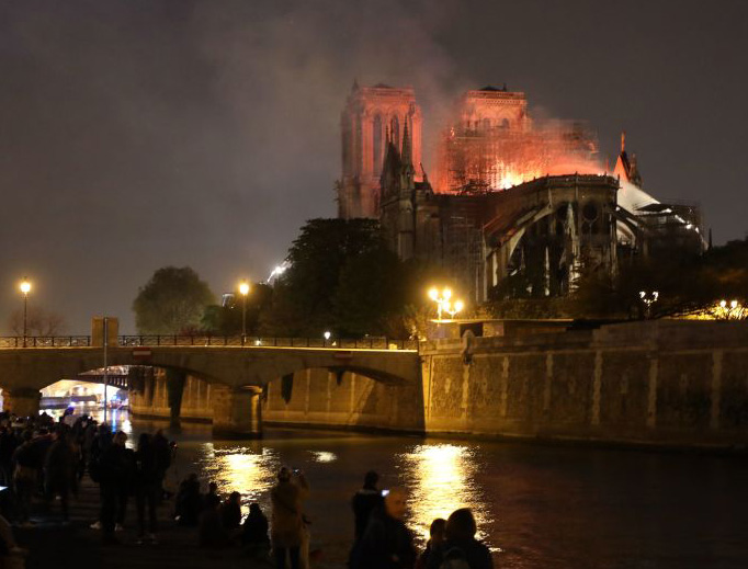 People stand on the banks of the River Seine as flames engulf the Notre-Dame Cathedral in Paris on April 15, 2019. People stand on the banks of the River Seine as flames engulf the Notre-Dame Cathedral in Paris on April 15, 2019.