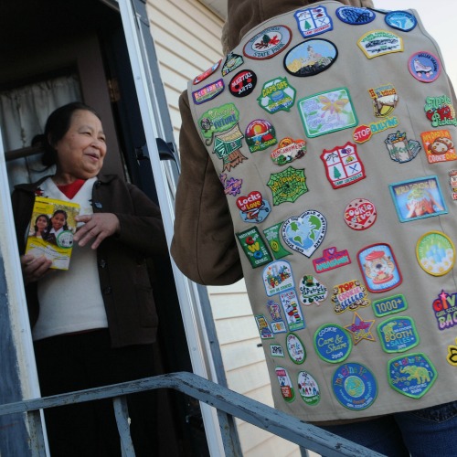 A Girl Scout, wearing her vest covered in badges, sells a box of cookies to a neighbor in Minneapolis. A Girl Scout, wearing her vest covered in badges, sells a box of cookies to a neighbor in Minneapolis.