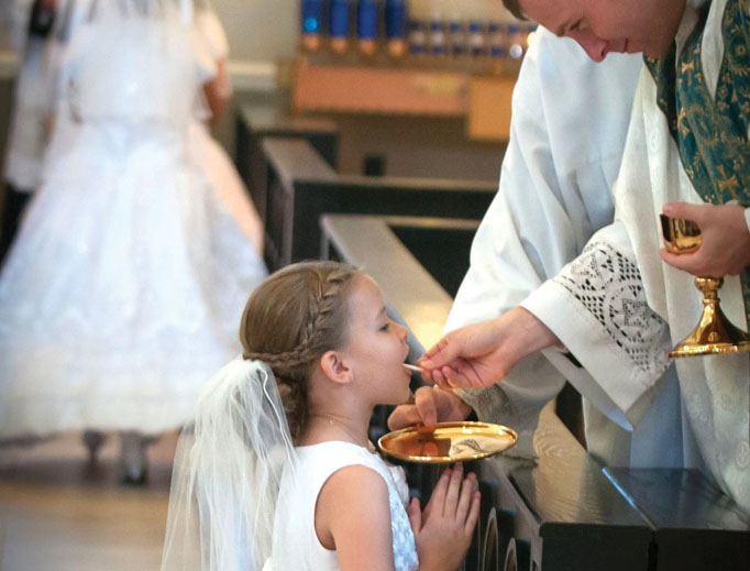 At Sacred Heart Church in Salisbury, North Carolina, first communicant Raegan Glenn receives Communion at the altar rail from Father John Eckert. At Sacred Heart Church in Salisbury, North Carolina, first communicant Raegan Glenn receives Communion at the altar rail from Father John Eckert.
