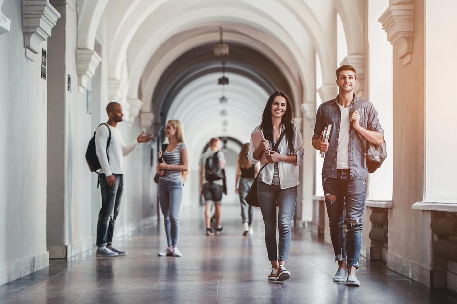 Students walking down a corridor on a college campus. Students walking down a corridor on a college campus.