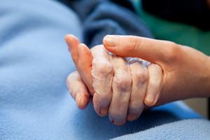 A woman holding the hand of an elderly person at a hospital. A woman holding the hand of an elderly person at a hospital.
