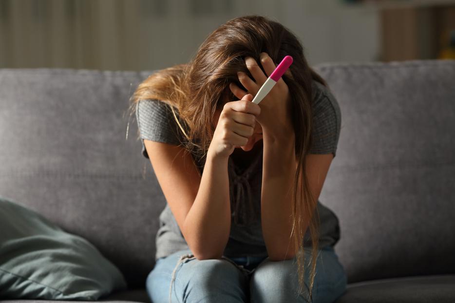 A woman sits holding a pregnancy test contemplating abortion. A woman sits holding a pregnancy test contemplating abortion.