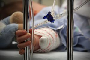 A child clasps metal bars of hospital bed. A child clasps metal bars of hospital bed.