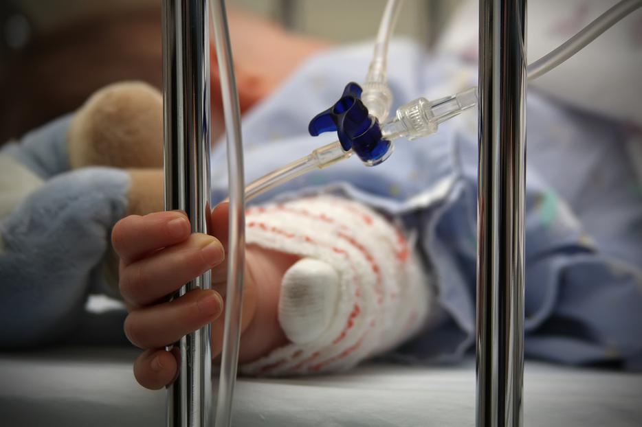 A child clasps metal bars of hospital bed. A child clasps metal bars of hospital bed.