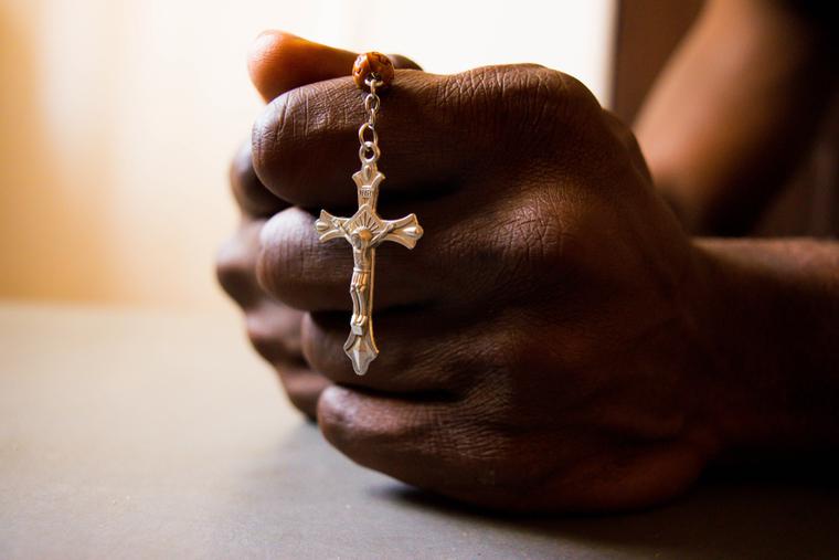 African man holds a crucifix while praying. African man holds a crucifix while praying.