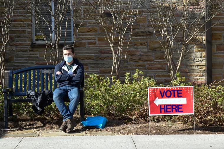A man sits next to a ‘vote’ sign outside on Jan. 5 in Atlanta during the Georgia Senate runoff elections. A man sits next to a ‘vote’ sign outside on Jan. 5 in Atlanta during the Georgia Senate runoff elections.