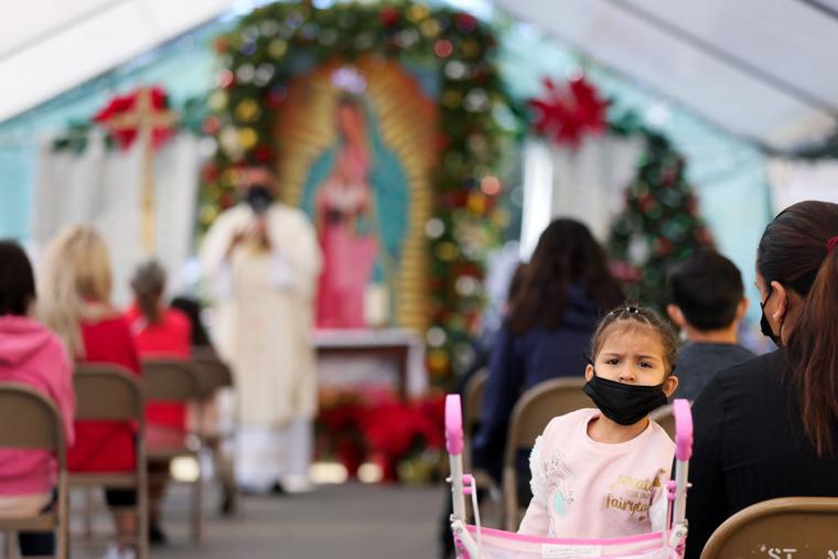 A girl wears a face covering as Father Rafael Saiz holds Christmas Mass outdoors at St. Mary's Catholic Church, which was held beneath a tent due to the COVID-19 pandemic, on December 25, 2020 in Los Angeles, California. A girl wears a face covering as Father Rafael Saiz holds Christmas Mass outdoors at St. Mary's Catholic Church, which was held beneath a tent due to the COVID-19 pandemic, on December 25, 2020 in Los Angeles, California.