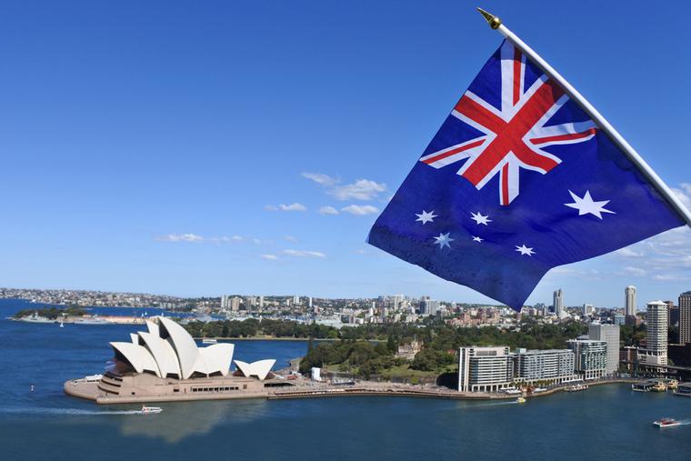 The National flag of Australia flies above the Sydney Harbor and the Opera house in Australia. The National flag of Australia flies above the Sydney Harbor and the Opera house in Australia.
