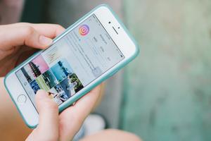 A woman holds a smartphone with the Instagram app displayed. A woman holds a smartphone with the Instagram app displayed.