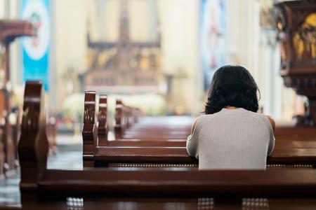 A woman sits kneeling in prayer inside a Catholic church.