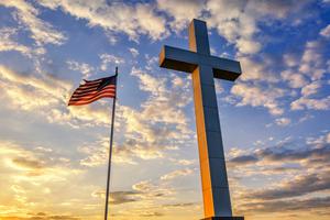 American flag waves in the wind alongside a cross. American flag waves in the wind alongside a cross.