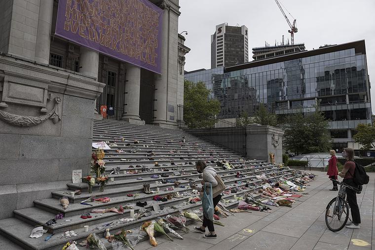 People place flowers and children's shoes at a memorial in Vancouver on May 30, 2021 People place flowers and children's shoes at a memorial in Vancouver on May 30, 2021