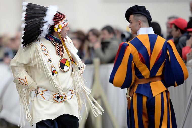 A Native American man wearing traditional regalia walks past a Swiss Guard during Pope Francis’ weekly general audience in St. Peter's Square at the Vatican on April 27, 2016. A Native American man wearing traditional regalia walks past a Swiss Guard during Pope Francis’ weekly general audience in St. Peter's Square at the Vatican on April 27, 2016.