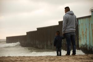 A father and son stand in front of the USA Mexico border wall at Tijuana. A father and son stand in front of the USA Mexico border wall at Tijuana.