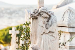 A statue of angel looks upon a grave inside a Catholic cemetery. A statue of angel looks upon a grave inside a Catholic cemetery.