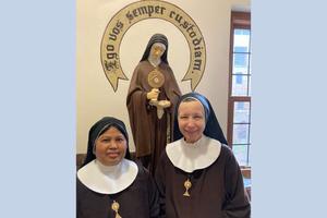 In the Adoration Monastery in Cleveland, Poor Clares Sister Mary Jacinta of the Immaculate Heart of Mary (l) and Sister Mary Joseph of the Most Precious Blood of Jesus stand before a statue of St. Clare, their order's foundress. The Latin phrase stenciled on the wall can be translated as ‘I will always defend you.’ In the Adoration Monastery in Cleveland, Poor Clares Sister Mary Jacinta of the Immaculate Heart of Mary (l) and Sister Mary Joseph of the Most Precious Blood of Jesus stand before a statue of St. Clare, their order's foundress. The Latin phrase stenciled on the wall can be translated as ‘I will always defend you.’